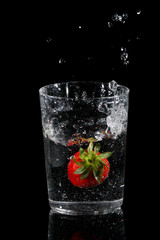 Strawberry falling into a glass of water and splashing on a black background