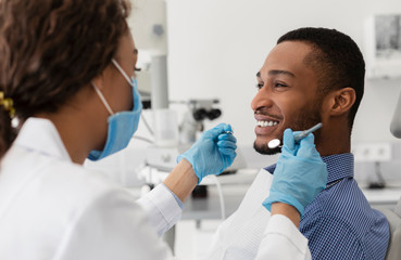 Young african guy smiling to his female dentist - obrazy, fototapety, plakaty