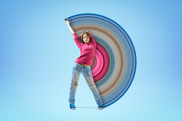 Young girl in pink hoodie and blue ripped jeans, standing with one arm raised and the other arm...