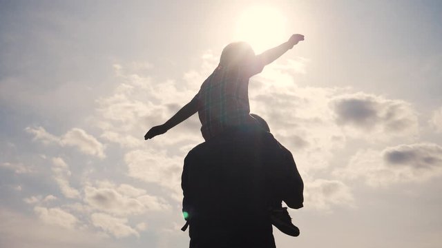 happy family silhouette teamwork concept slow motion video. son boy superhero sitting on his father man neck depicts a flight of an airplane playing a pilot. father and son silhouette at sunset nature