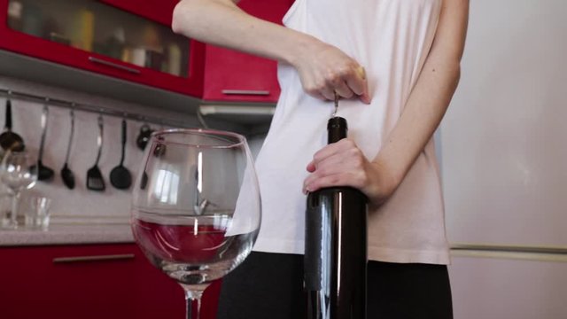 girl in a white shirt is trying to open a bottle of wine