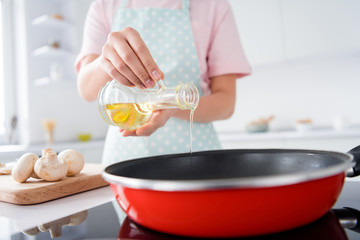 Cropped photo of beautiful housewife hold olive oil pouring hot frying pan enjoy hobby morning cooking tasty dinner family stand bright light kitchen indoors casual clothing