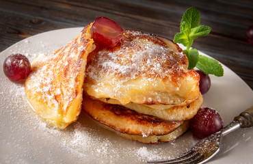 homemade pancakes with powdered sugar and grapes and mint on a dark wooden background, baking