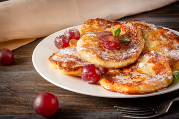 few sweet homemade pancakes with powdered sugar, grapes and mint, a beige towel on a wooden