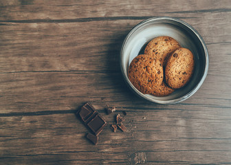 Homemade cookie Photo in rustic style Oatmeal cookies in a clay bowl and crumbled chocolate are lying on a wooden table