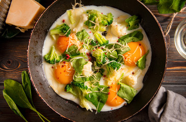 fried eggs with cheese ?broccoli, spinach, spices   in a pan on a dark wooden background, Breakfast, top view,  close up