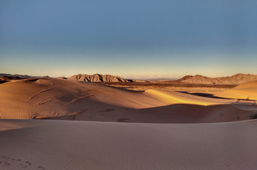 Fototapeta na wymiar Sand dunes in desert landscape at sunset with mountains