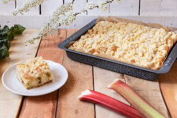 Kuchen mit Rhabarber und Streusel aus einem Blech auf einem Tisch aus hellem Holz