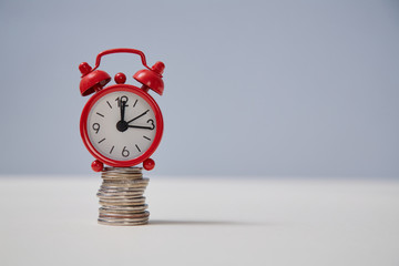 Time is money. Time-limit. Lack of time. Business deadline. Stack of coins and red alarm-clock on top, place for text