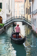 Fototapeta na wymiar Venice street vertical cityscape. Small Rio De Lalboro canal with a forged bridge Sotoportego de le Ostreghe over it and gondolier propels a gondola with tourists making guided tour. Italy, Europe.