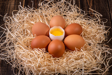 Fresh chicken eggs in a nest of hay on a wooden background.