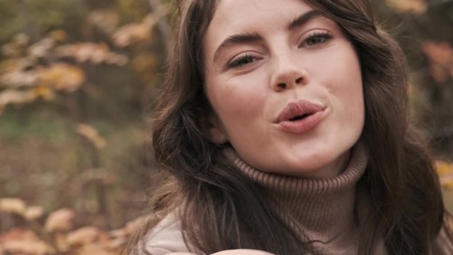 Young optimistic positive girl outdoors in green nature park looking camera blowing kisses