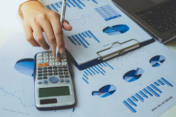 Close up of businessman hand holding pen while using calculator to calculate data on graph chart...