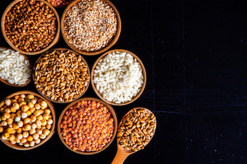 Bowls of various cereals. Various kinds of natural grains and cereals. Different types of groats in bowls on a black background. Healthy nutrition food