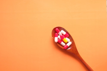 colorful capsule on spoon on orange background 