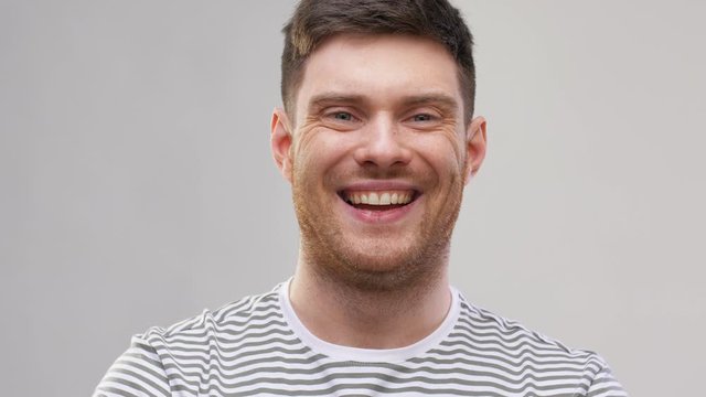 emotions and people concept - happy smiling young man in striped t-shirt over grey background