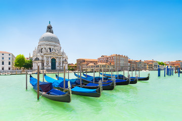 Fototapeta premium Panoramiczny piękny widok na tradycyjne weneckie gondole zacumowane w wodzie Canal Grande przed kościołem Basilica di Santa Maria della Salute, Wenecja, Włochy, w słoneczny dzień