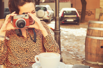 Trendy woman holding retro camera and drinking coffee outdoors.