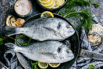 Frischer roher Dorado oder Seebrasse mit Spargel, Gewürzen, Kräutern, Zitrone und Salz auf dunklem Hintergrund.