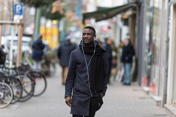 Young Black Man with Earphones Walking on Street and Looking Away