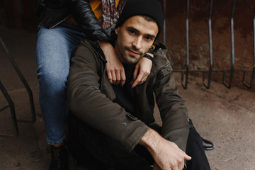 Obraz premium Handsome man with beard sitting on the road and woman hands on his shoulders
