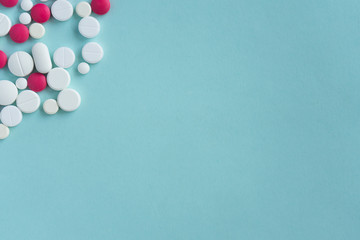 Medical concept. Blue background for text. Placer of multi-colored, white and pink tablets, pills of various shapes, on left side. Flatley, copyspace for pharmacies and pandemic content.