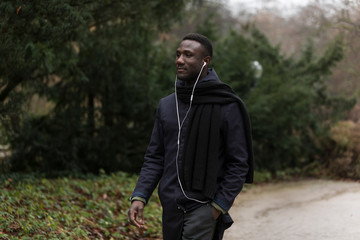 Young Black Man Walking Confidently with Earphones in Park