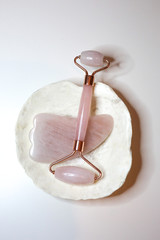Pink quartz face roller laying on the sea shell on white background. Beauty tools. Skin treatment...