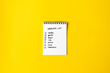 Grocery list paper notepad on yellow background with copy space, top view