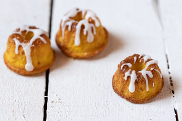kleiner gelber kuchen bzw gugelhupf aus zitronen mit zuckerguss auf weißem tisch aus brettern und holz