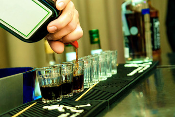 Bartender fill some glasses with alcohol .