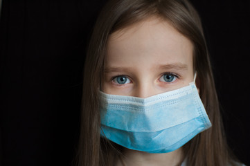 Studio portrait of little blond girl on black backgound in blue surgical disposable mask for protection of Coronavirus Covid-19 during self-isolation while stay home