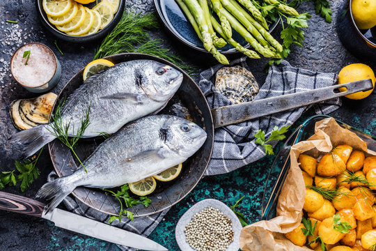 Fresh raw Dorado or sea bream with asparagus, spices, herbs, lemon and salt over dark background.