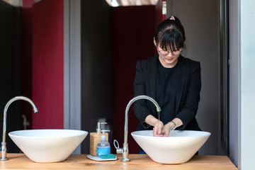 Asian young female in black business suit is washing her hand in front of outdoor toilet room.