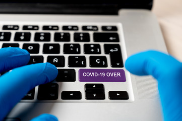 Covid-19 over words on keyboard button. End of coronavirus concept. A finger in a blue medical protective  glove pressing a colored button on notebook