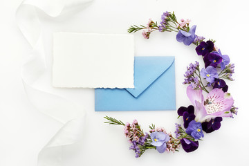 Blank white greeting card and envelope with purple wildflowers on white background for creative work design. Flat lay