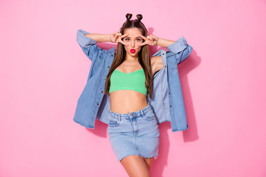 Photo of pretty funky tempting lady showing v-sign symbols near eyes blowing air kisses wear denim jacket green crop top short skirt isolated pastel pink color background