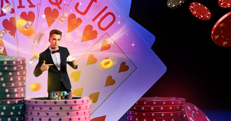 Man in suit pointing at two aces in his hand, posing against background with flying dollars and coins, playing cards, stacks of chips. Poker, casino