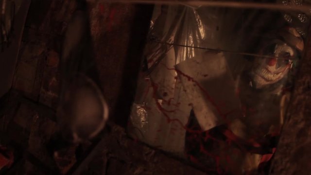 A scarier clown with knife at crude basement with a mirror on the wall