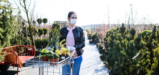 Young woman with face mask outdoors shopping in garden center, Corona virus concept.