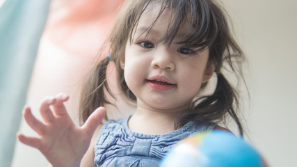 Happy playful toddler looking at globe ball on bed in bedroom at home.