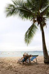 Young asian woman leisure relax on beach chair with floppy hat under the tree.