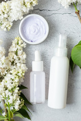 Fototapeta na wymiar Flat lay composition with white bottles. Mockup for organic natural products. Aromatic organic cosmetic products made from lilac flowers. Skin care concept.