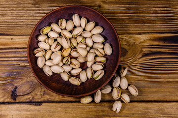 Obraz na płótnie Canvas Ceramic plate with pistachio nuts on a wooden table. Top view