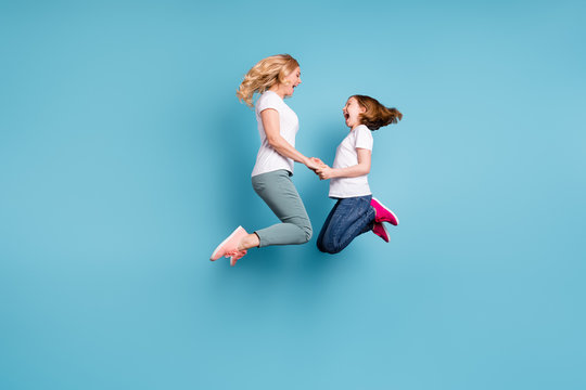 Full Length Profile Photo Of Funny Mom Lady Little Daughter Spend Time Together Jumping High Up Hold Hands Rejoicing Wear Casual White S-shirts Isolated Blue Color Background