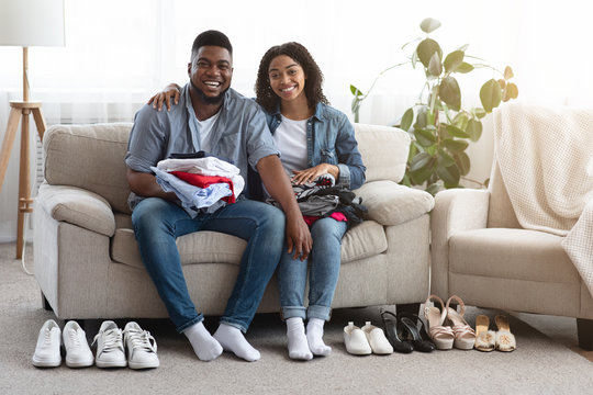 Changing Seasonal Clothes. Black Couple Posing With Neatly Arranged Shoes And Garment