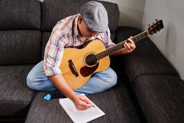 Middle-aged adult man. Wearing a cap and a plaid shirt on the sofa in his living room. Playing the...