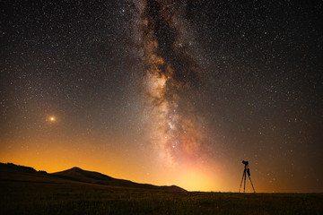 Beautfiul night landscape, silhouette of a camera on the tripod at the starry night and bright...