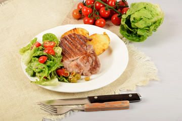 two pieces of grilled potato and grilled meat next to lettuce with tomatoes and olives on a white plate
