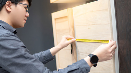 Asian man using tape measure on cabinet panel choosing materials or countertops for built-in...